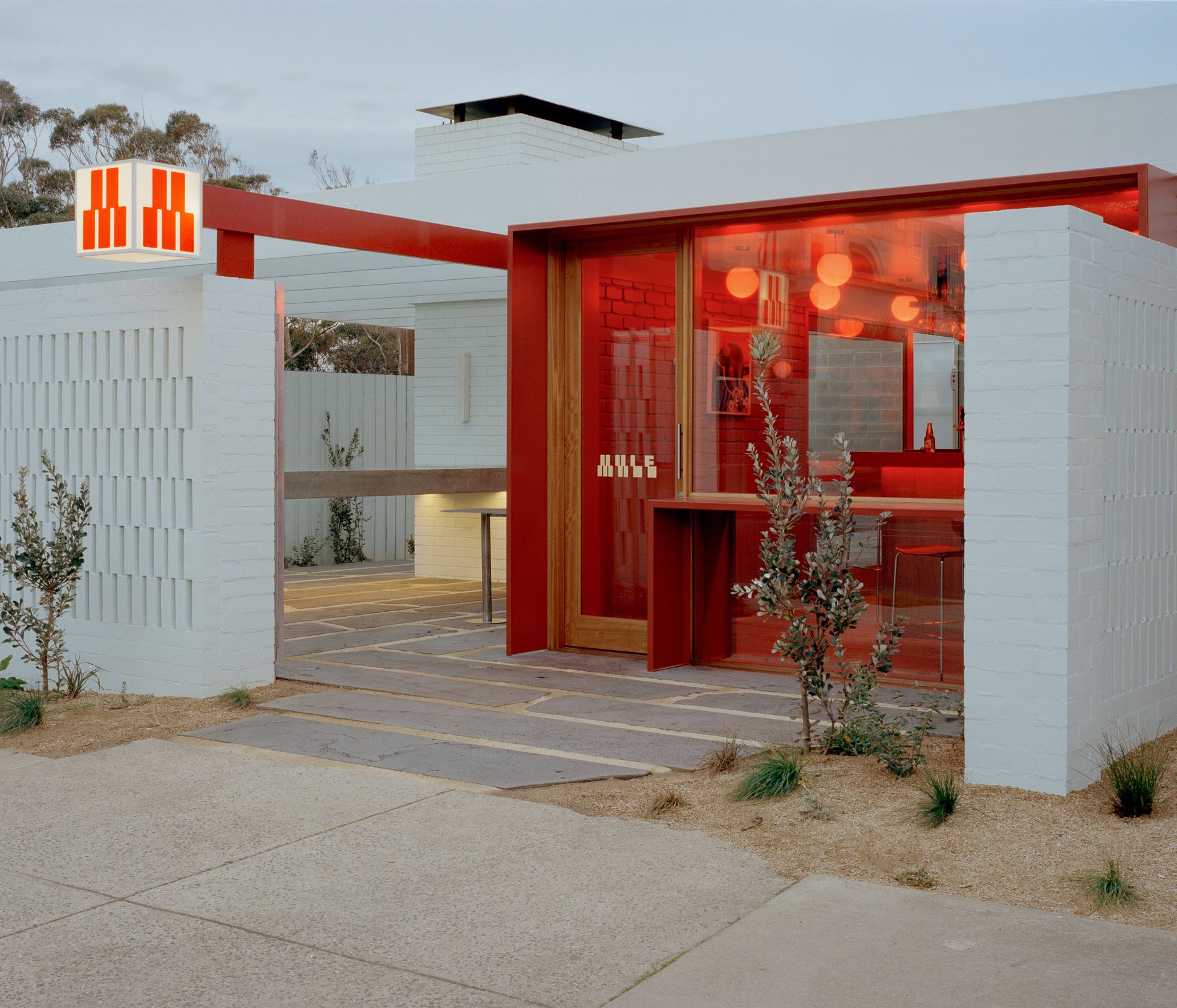 MULE entrance at dusk, the glowing red M sign above the breeze-block wall