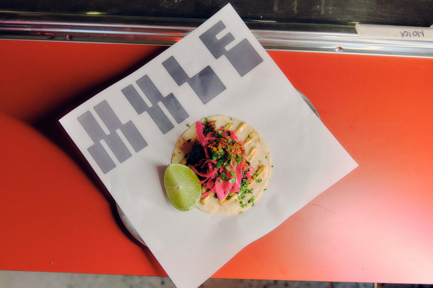 A MULE taco on branded paper with lime, pickled onion and herbs